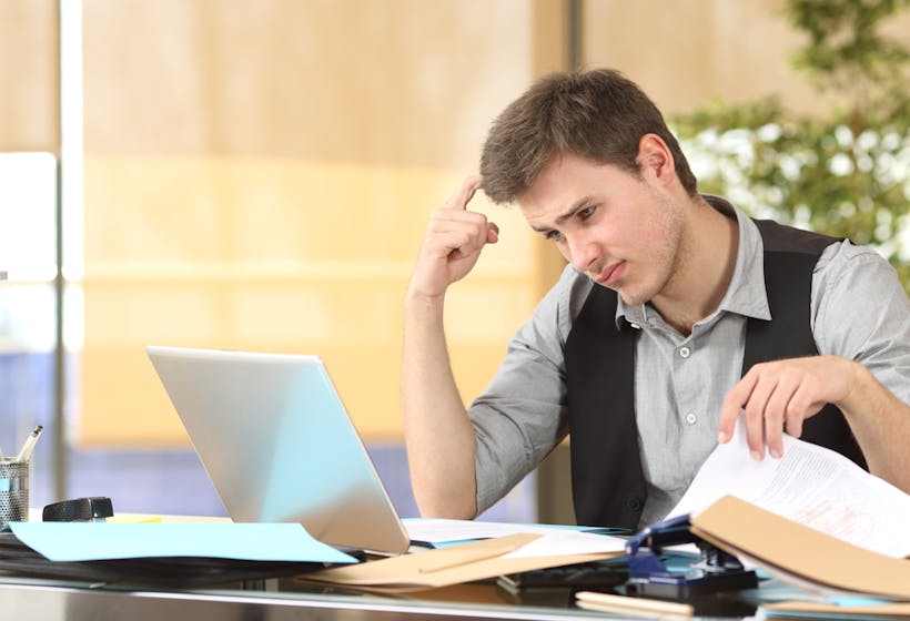 Incompetent employee thinking how to do his job online with messy desk at office.